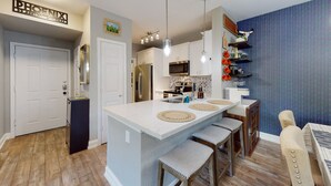 A modern kitchen with a central island, bar stools, and a blue patterned wall.