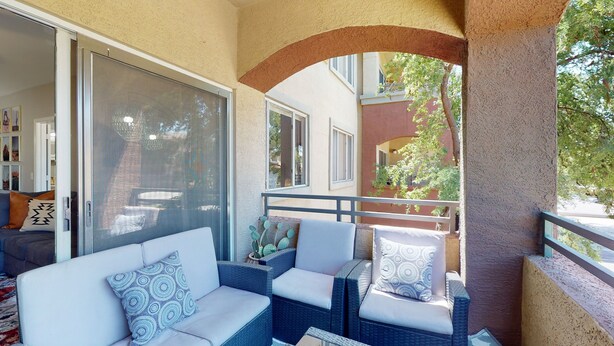 A balcony with wicker furniture, a glass door, and a view of a building with a red facade.