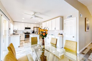 A modern kitchen with white cabinets, a glass dining table, and a ceiling fan. - WeeCasa | Dog-friendly house in Chandler with private heated pool, hot tub, AC (Chandler)