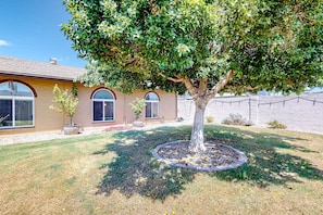 A house with a large tree in the front yard, a well-maintained lawn, and a clear sky. - WeeCasa | Dog-friendly house in Chandler with private heated pool, hot tub, AC (Chandler)