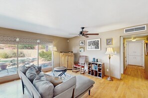 Uma sala de estar com sofá, poltrona de balanço, estante de livros e ventilador de teto.