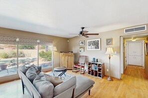 Un salón amplio con un sofá, un sillón mecedora, una estantería y un ventilador de techo.