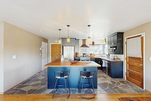 Una cocina amplia con una isla central, taburetes de bar, iluminación colgante y electrodomésticos modernos.