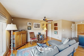 Una sala de estar con un sofá, un mueble de madera, una lámpara de pie, un ventilador de techo y una estantería.