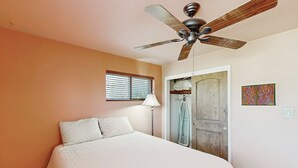 A bedroom with a bed, a ceiling fan, a window with blinds, a door, and a wall-mounted light fixture. - Sun-soaked & charming dog-friendly retreat with private pool, large patio, & W/D (Tucson)