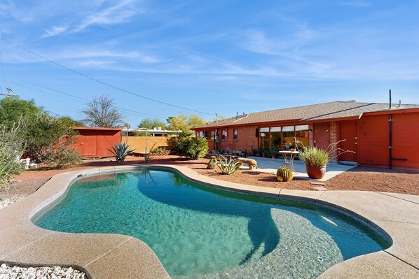 A residential property with a swimming pool, a red brick house, and a well-maintained garden.