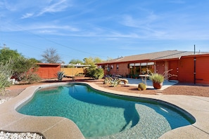 A residential property with a swimming pool, a red brick house, and a well-maintained garden.