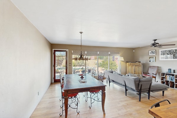 A spacious dining area with a wooden table and chairs, a chandelier, and a view of the outdoors through large windows.