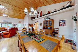 Ein geräumiges Wohnzimmer mit Holzboden, ein Essbereich mit einem langen Tisch und eine Küche im Hintergrund.