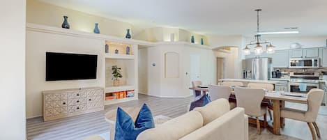 A modern living room with a flat-screen TV, a sofa, and a dining area with chairs and a table.