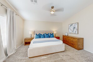 A bedroom with a bed, bedside tables, a dresser, a ceiling fan, and a painting on the wall. - Spacious desert home with hot tub, covered patio, grill, & modern finishes (Surprise)