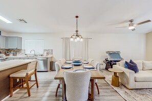A modern kitchen with a dining area, featuring a wooden dining table, white chairs, and a central chandelier. - Spacious desert home with hot tub, covered patio, grill, & modern finishes (Surprise)