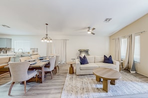 Ein modernes Wohnzimmer mit Essbereich, Deckenventilator und einer Küche im Hintergrund.