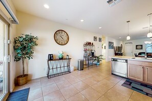 A modern kitchen with a dishwasher, a sink, and a countertop. There is a potted plant and a clock on the wall. - Airy desert home with an enclosed yard, private pool, hot tub, firepit, & W/D (Buckeye)