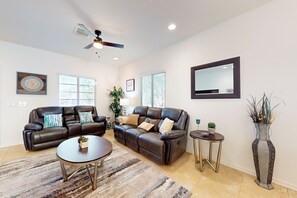 A modern living room with a leather sofa, a coffee table, and a floor lamp. - Airy desert home with an enclosed yard, private pool, hot tub, firepit, & W/D (Buckeye)