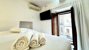Quarto de hotel com cama, toalhas dobradas, televisão de tela plana e janela com cortinas.