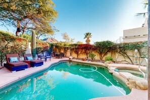 Une piscine entourée de chaises longues et d’une table, le tout bordé de verdure et avec une montagne en toile de fond.
