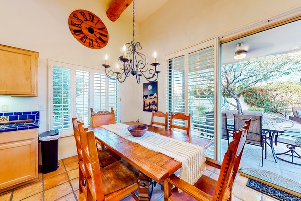A dining area with a wooden table, chairs, a chandelier, and a view of the outdoors.