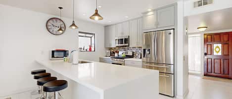 A modern kitchen with white cabinetry, stainless steel appliances, and a central island with bar stools.