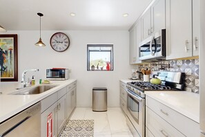 A modern kitchen with stainless steel appliances, a sink, and a window with a view. - Recently Remodeled Home | Fenced Backyard, Heated Pool, Grill & Fire Pit (Palm Springs)