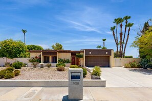 A modern house with a garage, surrounded by a well-maintained garden with various plants and a mailbox labeled "1980". - Recently Remodeled Home | Fenced Backyard, Heated Pool, Grill & Fire Pit (Palm Springs)