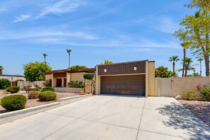 A modern two-story house with a garage, surrounded by landscaped gardens and palm trees. - Recently Remodeled Home | Fenced Backyard, Heated Pool, Grill & Fire Pit (Palm Springs)