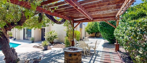 A covered patio area with a fire pit, outdoor furniture, and a swimming pool.
