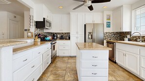 A modern kitchen with white cabinets, granite countertops, a stainless steel refrigerator, and a ceiling fan. - Updated mid-century gem with private pool, spa, gas grill, and free WiFi (Palm Springs)