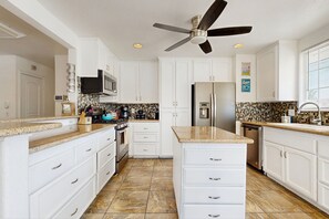 A modern kitchen with white cabinets, granite countertops, a stainless steel refrigerator, and a ceiling fan. - Updated mid-century gem with private pool, spa, gas grill, and free WiFi (Palm Springs)