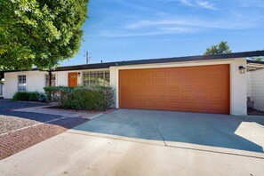 A single-story house with a garage, a front door, and a large tree to the left. - Updated mid-century gem with private pool, spa, gas grill, and free WiFi (Palm Springs)