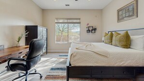 Ein Schlafzimmer mit einem Bett, einem Schreibtisch, einem Stuhl, einem Deckenventilator, einem Fenster und einer Tür.