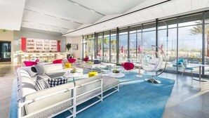 A modern lounge area with a large window, white sofas, colorful cushions, and a bar area with bottles. - Desert days, cozy nights, and poolside delights await at this stylish home. (Palm Springs)