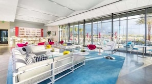 Ein stilvoller Lounge-Bereich mit großem Fenster, weißen Sofas, bunten Kissen und einer Bar mit Flaschen.
