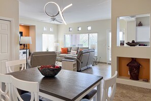A modern living room with a sofa, a dining table with chairs, a ceiling fan, and a large window. - Tastefully remodeled condo with pool, hot tub & fitness room (Oro Valley)