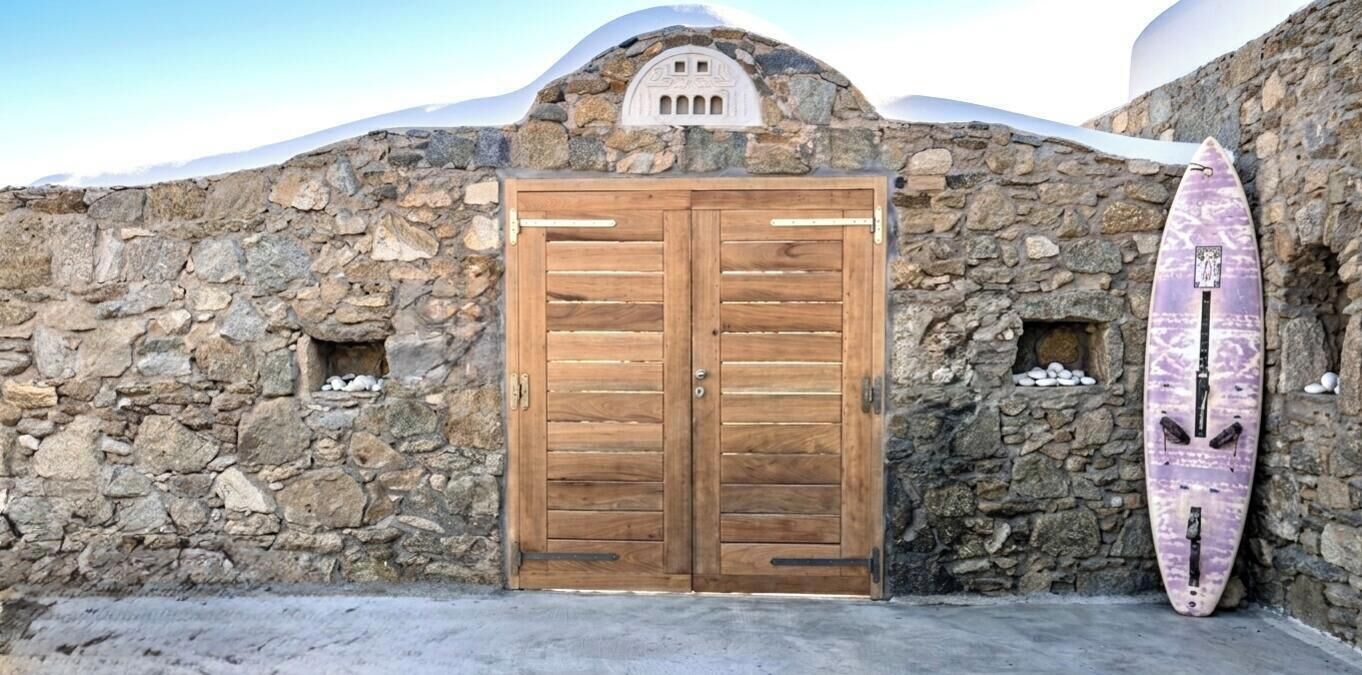 A stone building with a wooden double door and a surfboard leaning against it.