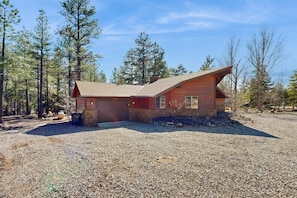 A cabin with a sloped roof, a stone foundation, and a gravel driveway. - Secluded dog-friendly home with gas grill, patio, wood-burning fireplace, & W/D (Munds Park)