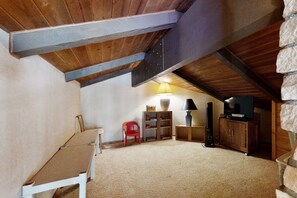 Ein gemütliches Dachzimmer mit schrägem Dach, einem roten Sessel, einer Holzkommode und einem Fernseher.
