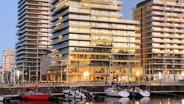 Ein modernes Hochhaus mit mehreren Balkonen und einer Marina, vor der Boote vor Anker liegen.