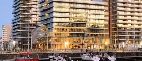 Un immeuble moderne de grande hauteur, doté de nombreux balcons, et une marina où sont amarrés des bateaux.