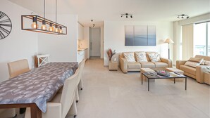 Ein modernes Wohnzimmer mit Essbereich, einer Sofagarnitur und einem Couchtisch. Im Hintergrund befindet sich eine Küche mit Spüle und Schränken.
