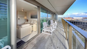 Ein Balkon mit einer Couch und Stühlen, Blick auf die Stadt und ein Holzboden.