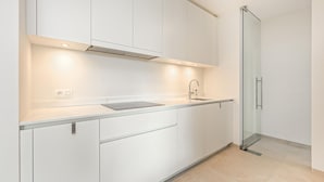 Eine moderne Küche mit weißen Schränken, einer Spüle aus Edelstahl und einer Glastür zum Badezimmer.