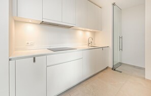 A modern kitchen with white cabinetry, a stainless steel sink, and a glass door leading to a bathroom. - Cozy apartment in Oostende with harbor view (Oostende)