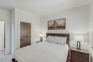 Une chambre à coucher avec un grand lit, deux tables de chevet avec des lampes, une porte en bois et un tableau encadré au mur.