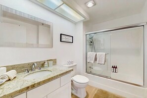Une salle de bain moderne avec une douche à parois de verre, des toilettes blanches et un lavabo sur un plan de travail en granit.
