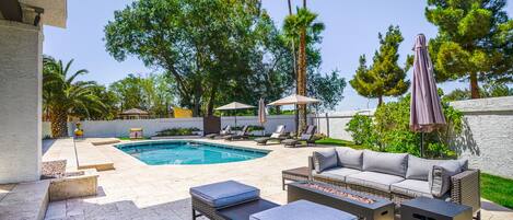 A backyard with a swimming pool, outdoor furniture, and a patio area.