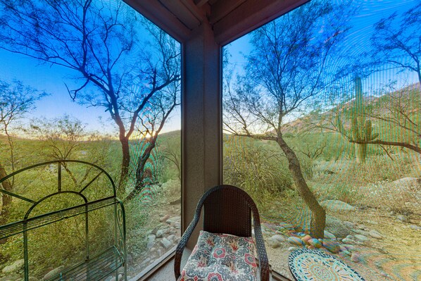 A room with a wicker chair and a patterned table, a window with a view of trees and a desert landscape. - Darling Desert Oasis with Fast WiFi, Shared Pool, Hot Tub, & Fitness Center (Tucson)