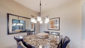 Une salle à manger avec une table en marbre, des chaises en cuir, un lustre et des œuvres d’art encadrées accrochées aux murs.