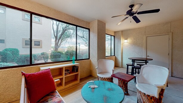 Une pièce dotée d’une grande fenêtre, d’un ventilateur de plafond, d’un banc en bois, d’une petite table et de deux chaises.