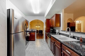 A modern kitchen with stainless steel appliances, wooden cabinets, a granite countertop, and a central island. - Dog-friendly mountain view condo with pool, gym, grill, fireplace, & sunroom (Tucson)